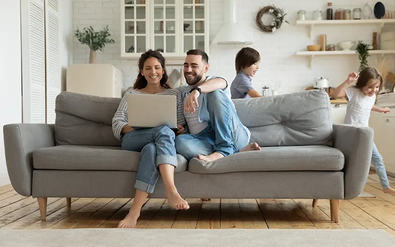 A man and woman sat on sofa looking at laptop.