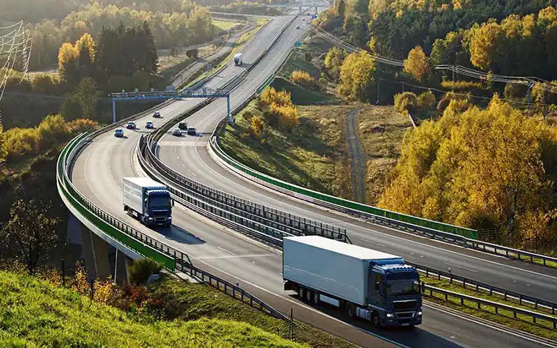 lorries and cars driving on a road in picturesque landscape