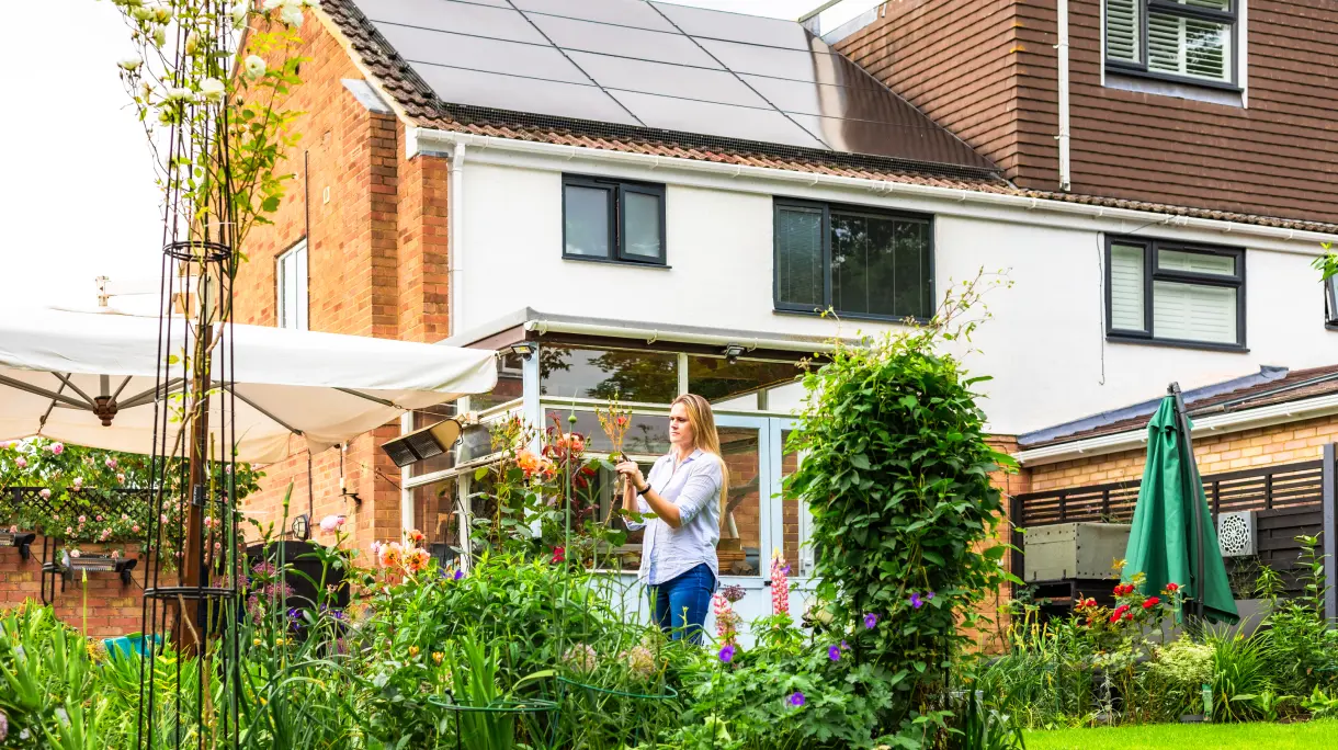 Homeowner in garden with solar panels on house roof
