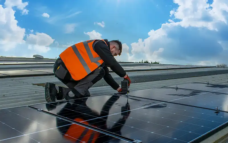 A man wearing an orange hi-vis jacket installing solar panels on a commercial building.